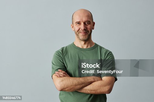 Minimal waist up portrait of mature bald man smiling at camera while standing confidently with arms crossed, copy space